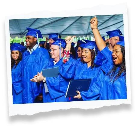 Group of adult graduates wearing blue caps and gowns celebrating and raising their hands at a graduation ceremony