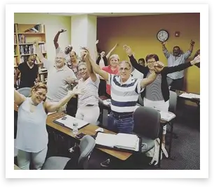 group of adult students raising their hands in the air in a classroom setting