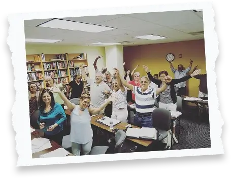 group of adult students raising their hands in the air in a classroom setting