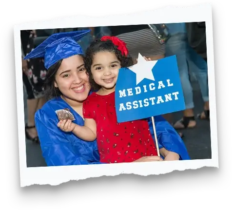 woman wearing a blue graduation cap and gown holding her toddler daughter and a sign that reads "Medical Assistant"
