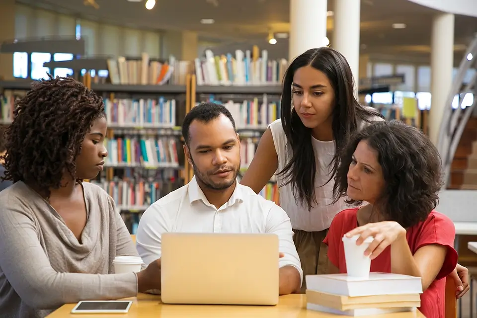 Diverse group of students looking at a computer screen with their teacher inside the library